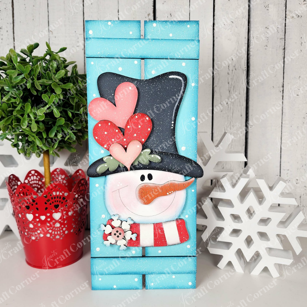 The Valentine Snowman Table Top Pallet Shelf Leaner by Janet's Craft Corner is a DIY winter decor kit featuring a smiling snowman in a black hat with hearts, blue background with white dots, red plant pot, and a white snowflake. Set of 1.