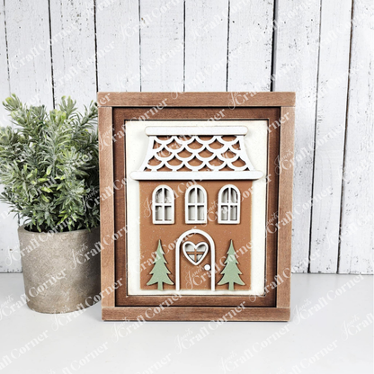 Decorative house-shaped cutout with a wooden frame on a white surface with a plant.