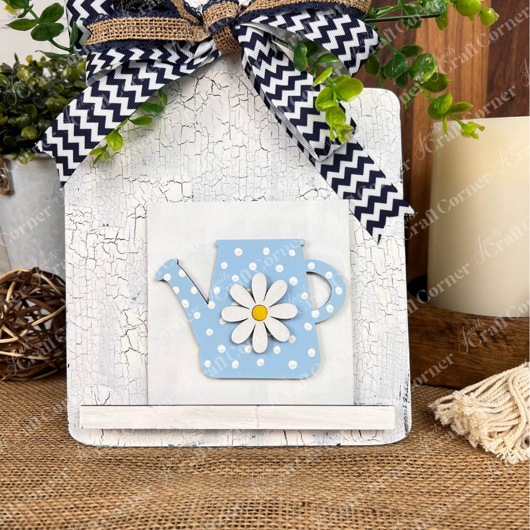 The Bloom & Grow Squares sign by Janet's Craft Corner features a blue polka-dot teapot with daisy design, cracked white finish, greenery, chevron bow, and rustic accents—perfect décor for tiered trays or small spaces.
