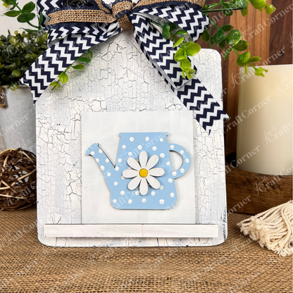 The Bloom & Grow Squares sign by Janet's Craft Corner features a blue polka-dot teapot with daisy design, cracked white finish, greenery, chevron bow, and rustic accents—perfect décor for tiered trays or small spaces.