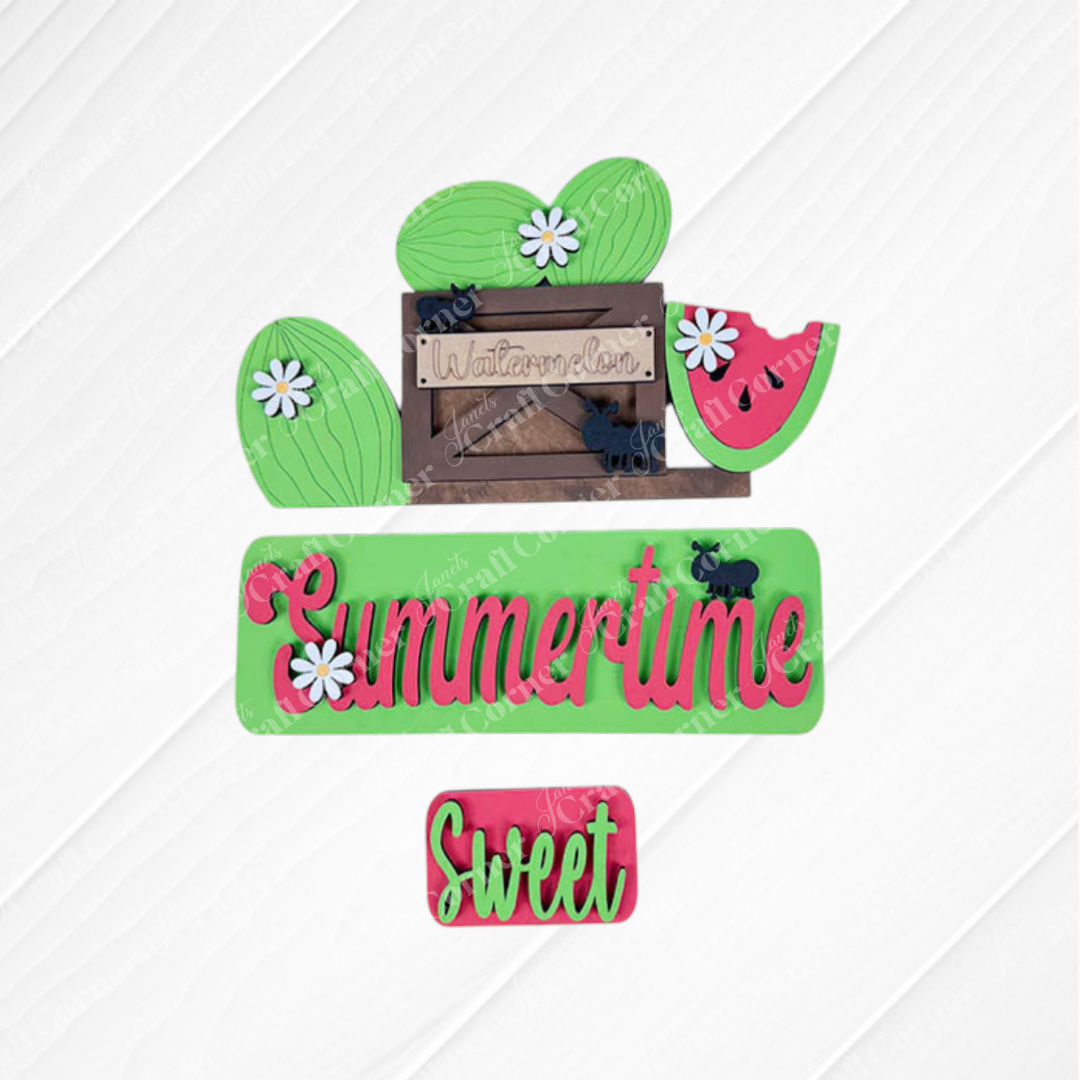 Decorative pieces from Janet's Craft Corner are arranged on a textured white square with a burlap background. The Summertime Watermelon Interchangeable Insert features a wooden watermelon sign alongside green and red "Summertime" and "Sweet" cutouts, small daisies, and hand-painted black elephant shapes for the perfect summer flair.