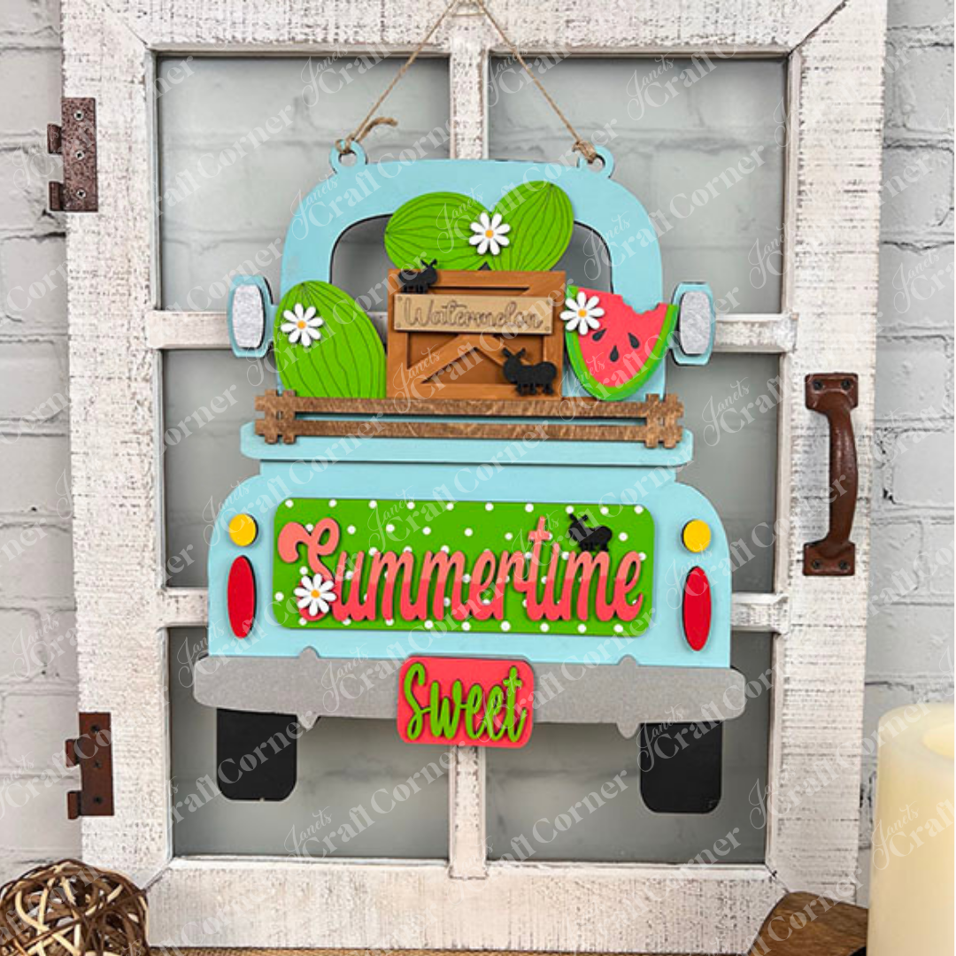 This delightful piece from Janet's Craft Corner, the Summertime Watermelon Interchangeable Insert - Painted, showcases a decorative wall hanging with a vintage truck brimming with watermelons and a "Summertime Sweet" sign. The hand-painted ornaments add charm as the truck is mounted on a rustic whitewashed wooden frame, decorated with tiny ant figurines on the watermelons.