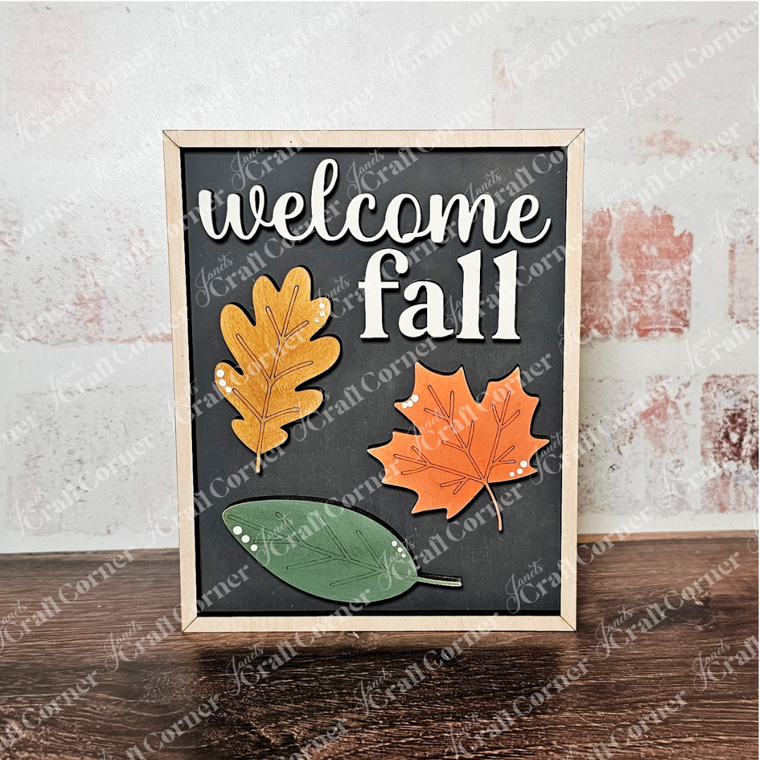 Janet's Craft Corner Fall in the Forest Switchable Farmhouse Signs DIY kit includes a framed "welcome fall" sign with yellow, orange, and green leaves on black—ideal for woodland or classic farmhouse seasonal decor. Choice of 3 designs.