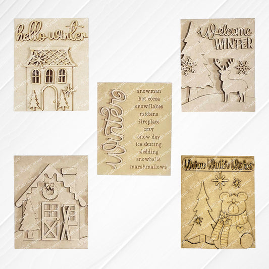 Displayed on a white wood backdrop are three winter-themed decorations: Janet's Craft Corner's Welcome Winter farmhouse signs featuring a deer, a polar bear, a list of winter words, a Victorian house and a house adorned with snow and skis. These items make for perfect home decor pieces.