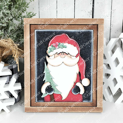 Janet's Craft Corner's North Pole Switchable Farmhouse Signs features Santa holding a green Christmas tree with snowy accents and pine branches—a festive DIY kit for seasonal home decor.