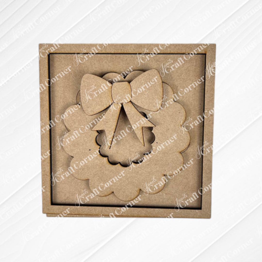 The Merry Christmas Squares by Janet's Craft Corner features a square, unfinished MDF wreath with a bow inside a matching frame—ideal for DIY holiday decor or adding to your Swappable Square Displays craft kit.