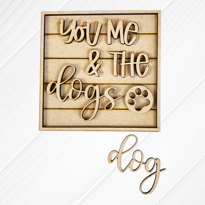 Janet's Craft Corner Dog Squares: Wooden cutout sign says "You Me & The Dogs" with a paw print. Features wood accents on a slatted background and "dog" displayed below on a white surface—perfect for tiered tray decor.