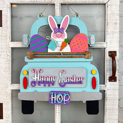 This charming Easter Bunny Interchangeable Insert from Janet's Craft Corner, an ideal DIY home decor kit, showcases a lively blue truck carrying a bunny, eggs, and a carrot. With "Happy Easter" and "Hop" embellishments, it beautifully adorns a rustic white door.