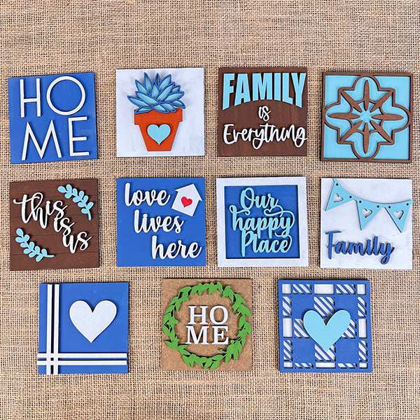 Introducing the Home Family Interchangeable Squares by Janet's Craft Corner, a delightful collection of mini signs showcasing diverse designs and messages such as "HOME," "Family is Everything," and "Love lives here." These pieces feature primarily blue and brown hues with heart and floral motifs on a textured background, ideal for adding charm to your home decor.