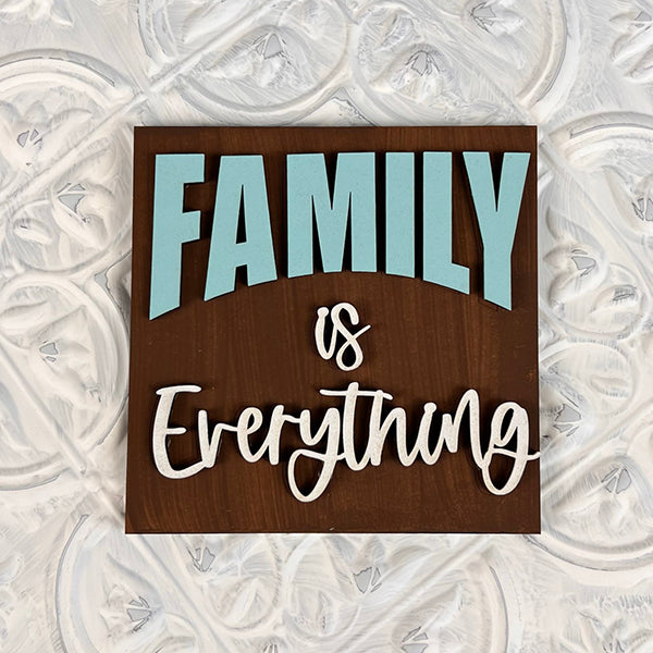 Introducing a delightful addition to your home decor, the *Home Family Interchangeable Squares* by Janet's Craft Corner. This wooden sign prominently features the word "Family" in bold, light blue letters, contrasting beautifully with the cursive white script of "is Everything." Its textured white and gray background adds a cozy warmth to any room.